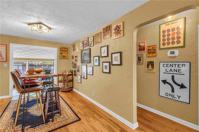 dining room with light wood finished floors, a textured ceiling, a textured wall, arched walkways, and baseboards