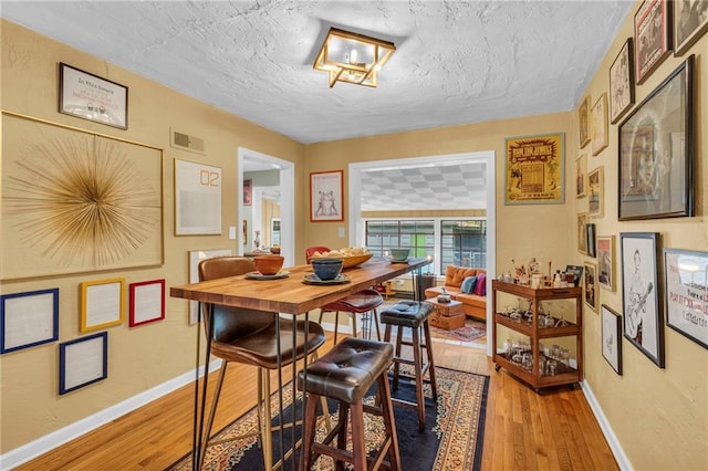 dining room with light wood-style floors, baseboards, and a textured ceiling