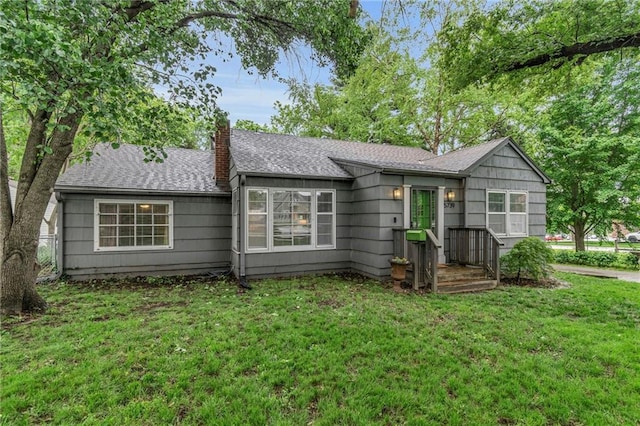 view of front of home with a chimney, a front yard, and roof with shingles