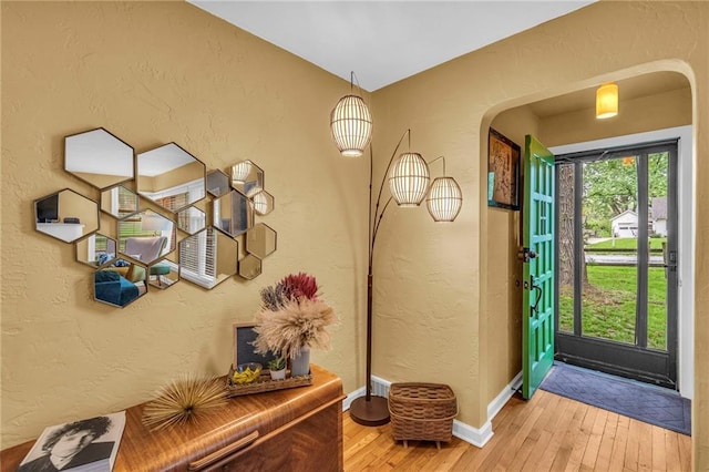 entryway featuring arched walkways, light wood-type flooring, a textured wall, and baseboards