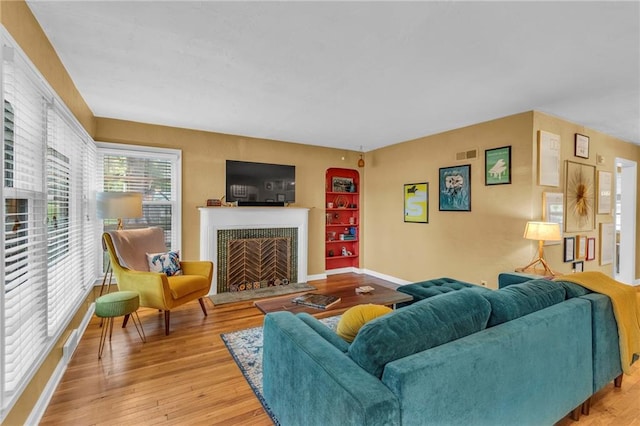 living area featuring a fireplace with raised hearth, light wood-style flooring, and baseboards