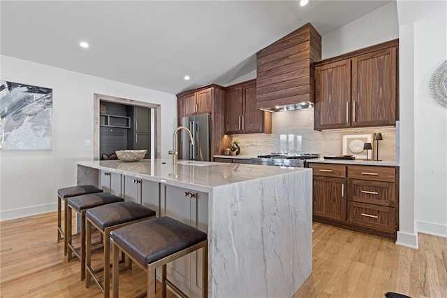 kitchen featuring a kitchen breakfast bar, backsplash, high quality fridge, vaulted ceiling, and an island with sink