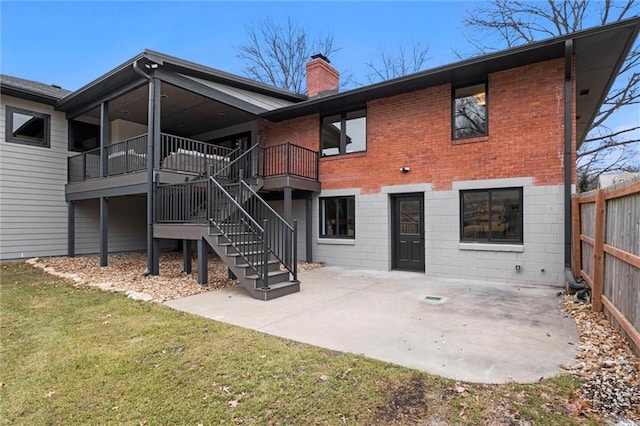 rear view of house featuring a patio, a yard, a chimney, brick siding, and fence