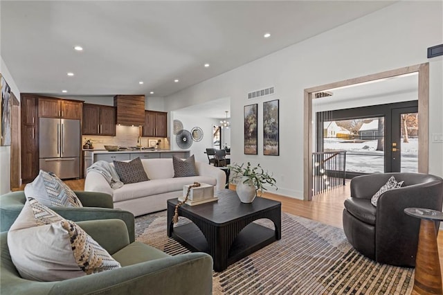 living area featuring recessed lighting, an inviting chandelier, light wood finished floors, baseboards, and visible vents