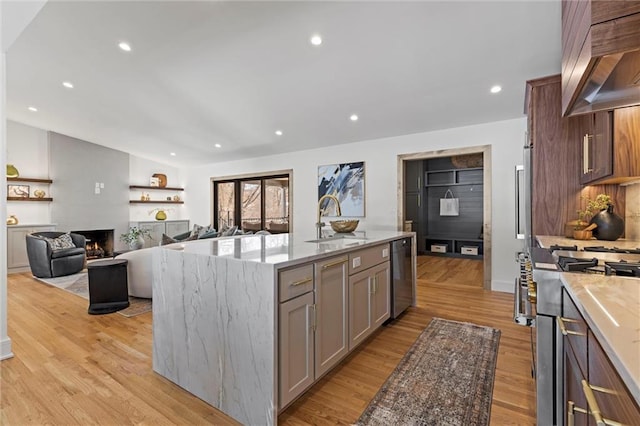 kitchen with gray cabinets, stainless steel appliances, wall chimney range hood, a sink, and light wood-type flooring