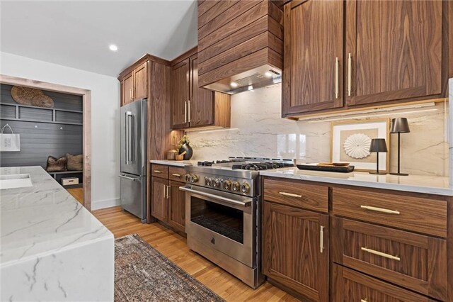 kitchen featuring tasteful backsplash, light stone countertops, custom range hood, light wood-type flooring, and premium appliances