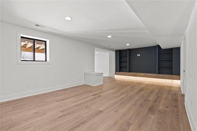 basement featuring light wood-style flooring, visible vents, built in features, and baseboards