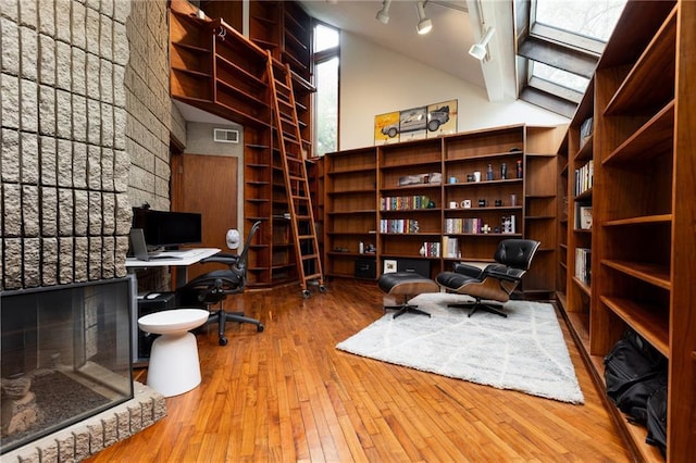 home office featuring hardwood / wood-style floors, visible vents, lofted ceiling with skylight, and track lighting