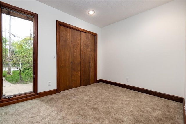 unfurnished bedroom featuring baseboards, carpet floors, a textured ceiling, and a closet