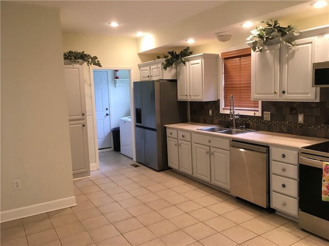 kitchen with appliances with stainless steel finishes, a sink, white cabinetry, washer / dryer, and tasteful backsplash