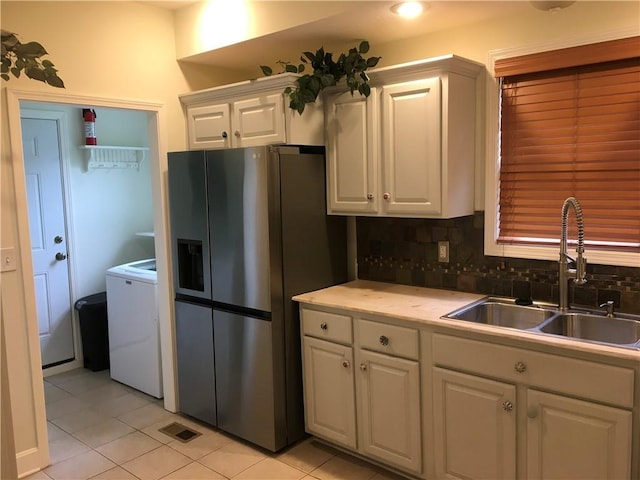kitchen featuring stainless steel refrigerator with ice dispenser, washer / clothes dryer, a sink, light tile patterned floors, and white cabinetry
