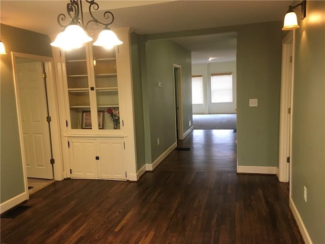 unfurnished dining area with baseboards, dark wood-style flooring, a chandelier, and visible vents