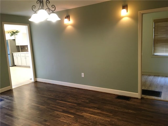 unfurnished room with baseboards, dark wood finished floors, a notable chandelier, and visible vents
