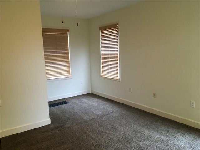 unfurnished room with visible vents, baseboards, dark carpet, and a healthy amount of sunlight