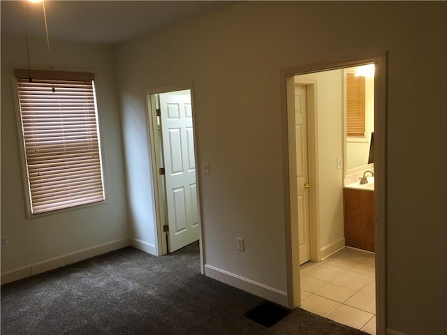 unfurnished bedroom with a sink, baseboards, light tile patterned floors, and light colored carpet