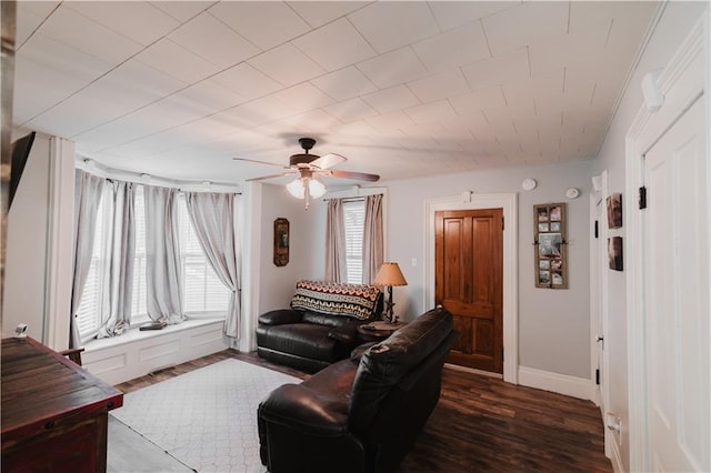 living area with baseboards, a ceiling fan, and dark wood-style flooring