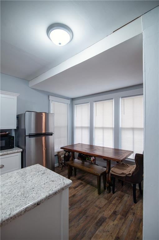 kitchen with dark wood-style flooring, black microwave, light stone counters, freestanding refrigerator, and white cabinetry