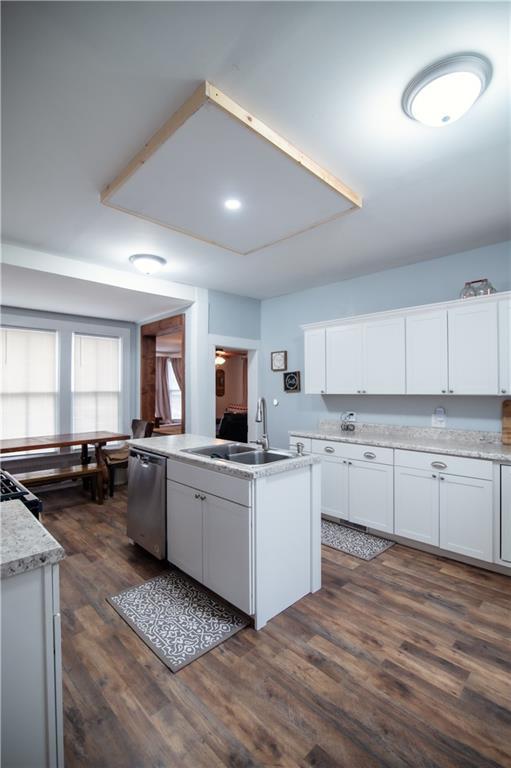 kitchen featuring stainless steel dishwasher, a kitchen island with sink, dark wood-style floors, white cabinets, and a sink
