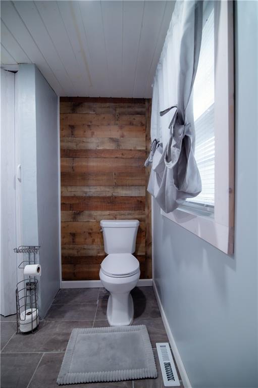 bathroom with wooden walls, toilet, visible vents, and wooden ceiling