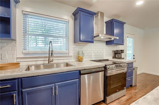 7636 Windsor St, Prairie Village, KS 66208 - kitchen featuring wall chimney exhaust hood, blue cabinetry, and appliances with stainless steel finishes