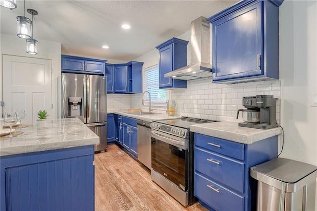 7636 Windsor St, Prairie Village, KS 66208 - kitchen with wall chimney range hood, appliances with stainless steel finishes, a sink, blue cabinetry, and light wood-style flooring