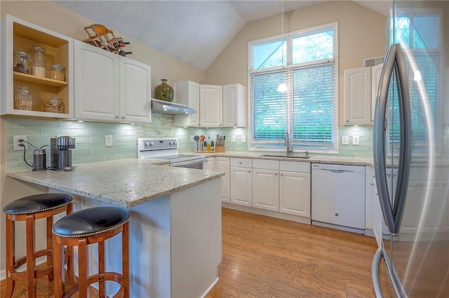 kitchen with white appliances, under cabinet range hood, a sink, a peninsula, and white cabinets