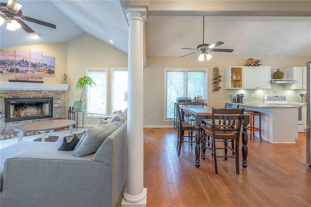 dining room featuring ceiling fan, vaulted ceiling, wood finished floors, a fireplace, and decorative columns