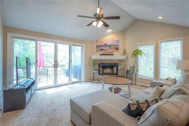 living room featuring carpet flooring, a ceiling fan, vaulted ceiling, a fireplace with raised hearth, and a textured ceiling