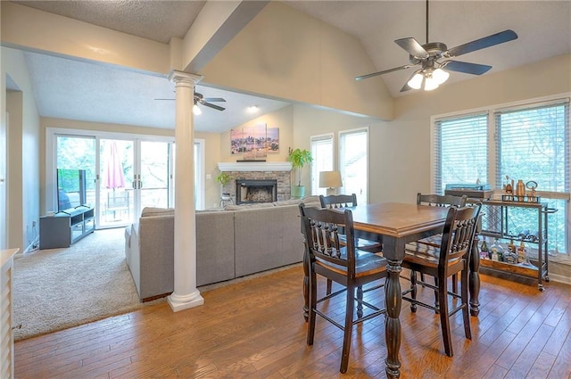 dining area featuring a ceiling fan, a fireplace, decorative columns, hardwood / wood-style floors, and vaulted ceiling