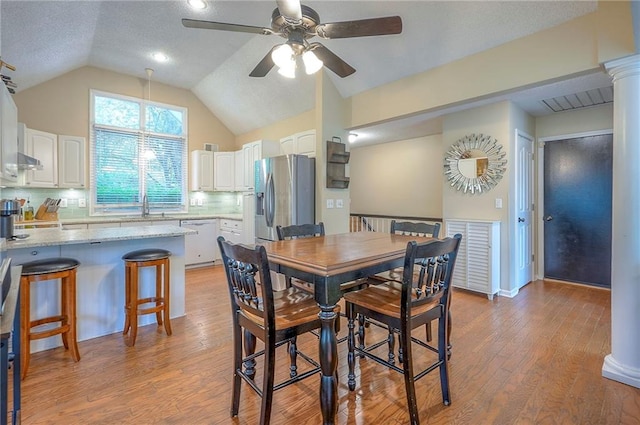 dining room with ceiling fan, vaulted ceiling, light wood-type flooring, and a textured ceiling