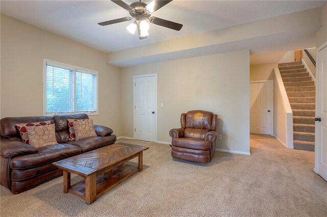 living area featuring light colored carpet, stairs, ceiling fan, and baseboards