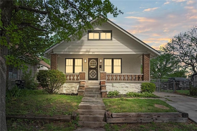 bungalow-style home featuring fence, covered porch, and brick siding