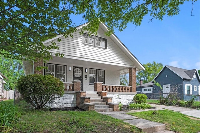 bungalow-style house with a porch, brick siding, and fence