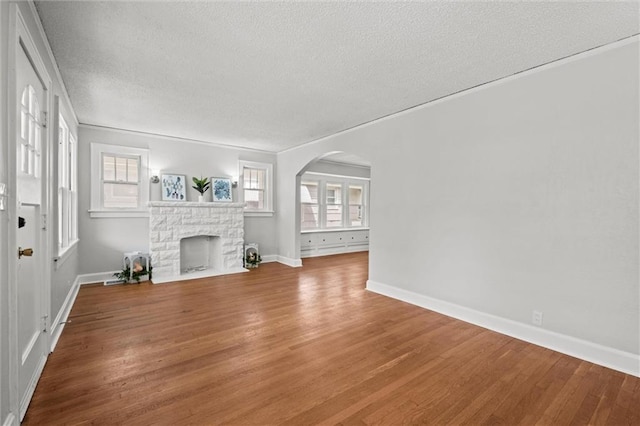 unfurnished living room featuring a fireplace, arched walkways, a textured ceiling, baseboards, and wood finished floors