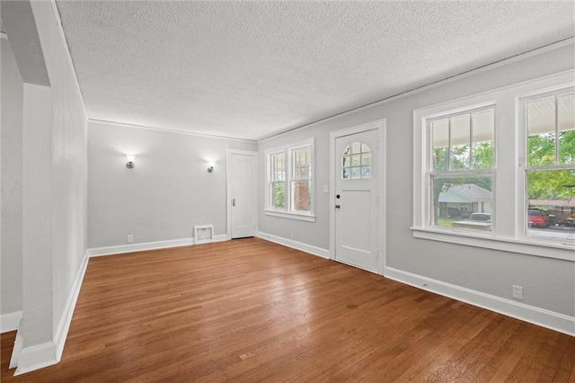 foyer with baseboards, visible vents, a textured ceiling, and wood finished floors