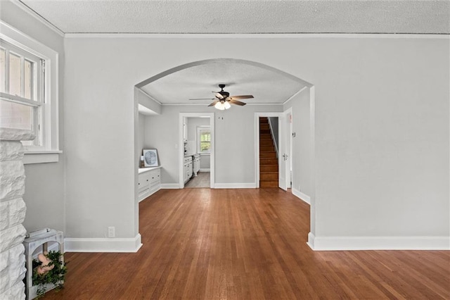 interior space featuring arched walkways, stairs, a ceiling fan, baseboards, and wood finished floors