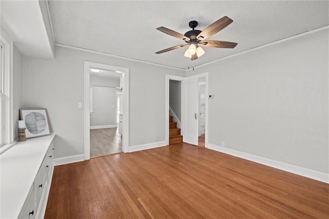 unfurnished bedroom featuring a textured ceiling, baseboards, a ceiling fan, and wood finished floors