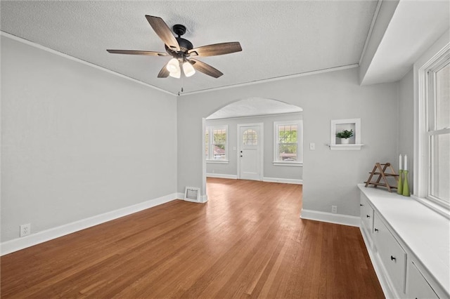 unfurnished living room with ceiling fan, a textured ceiling, visible vents, arched walkways, and wood finished floors