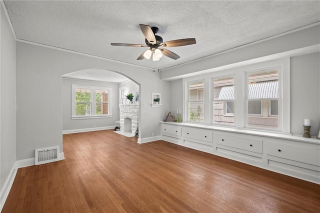empty room with a fireplace, arched walkways, a textured ceiling, wood finished floors, and visible vents