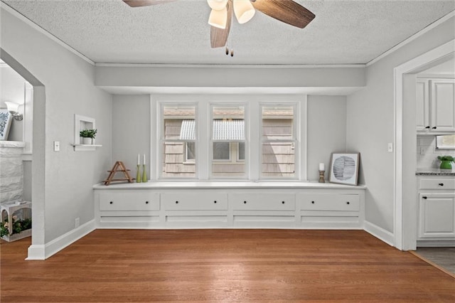 interior space with a textured ceiling, ceiling fan, baseboards, and wood finished floors