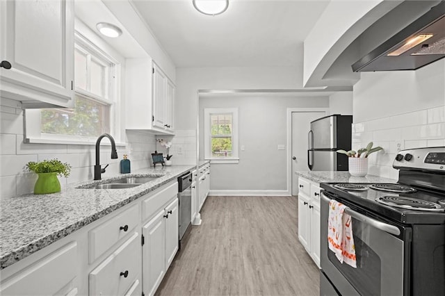 kitchen featuring wall chimney range hood, white cabinets, a sink, stainless steel appliances, and backsplash