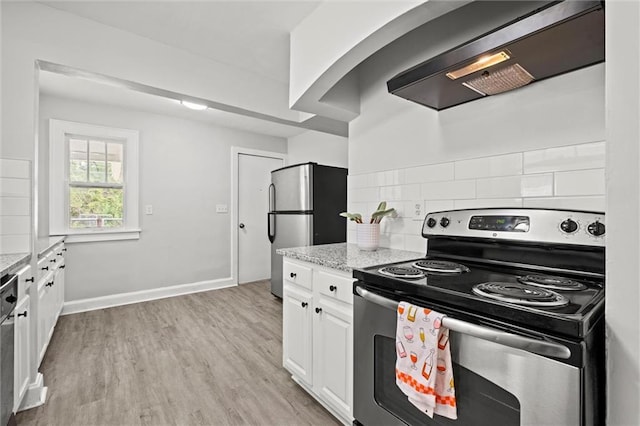 kitchen featuring decorative backsplash, wall chimney exhaust hood, white cabinets, light stone counters, and appliances with stainless steel finishes