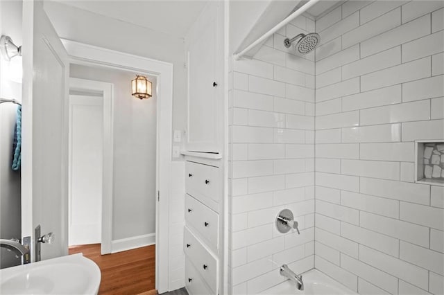 full bath featuring baseboards, bathing tub / shower combination, a sink, and wood finished floors