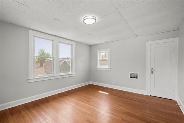 empty room with visible vents, baseboards, wood finished floors, and a drop ceiling