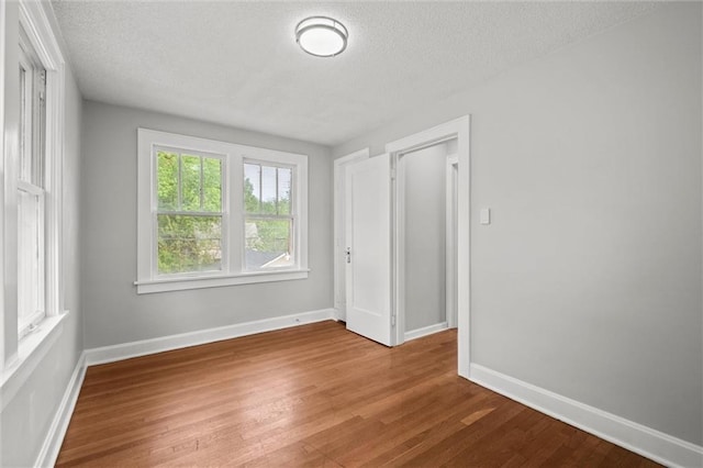 spare room with baseboards, a textured ceiling, and wood finished floors