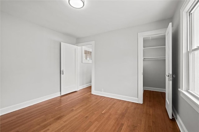 unfurnished bedroom featuring a walk in closet, baseboards, a closet, and wood finished floors