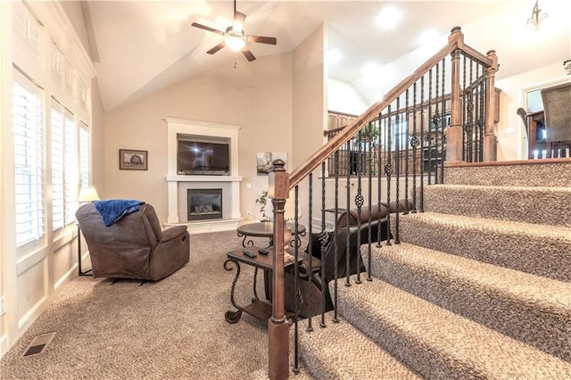 stairs featuring carpet floors, a glass covered fireplace, a ceiling fan, vaulted ceiling, and visible vents