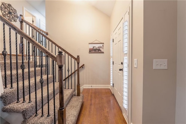 foyer featuring baseboards, wood finished floors, vaulted ceiling, and stairway