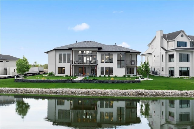 back of house with a balcony, a water view, stucco siding, and a yard