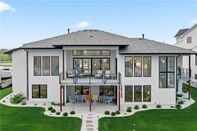 rear view of house featuring stucco siding, a lawn, roof with shingles, and a balcony